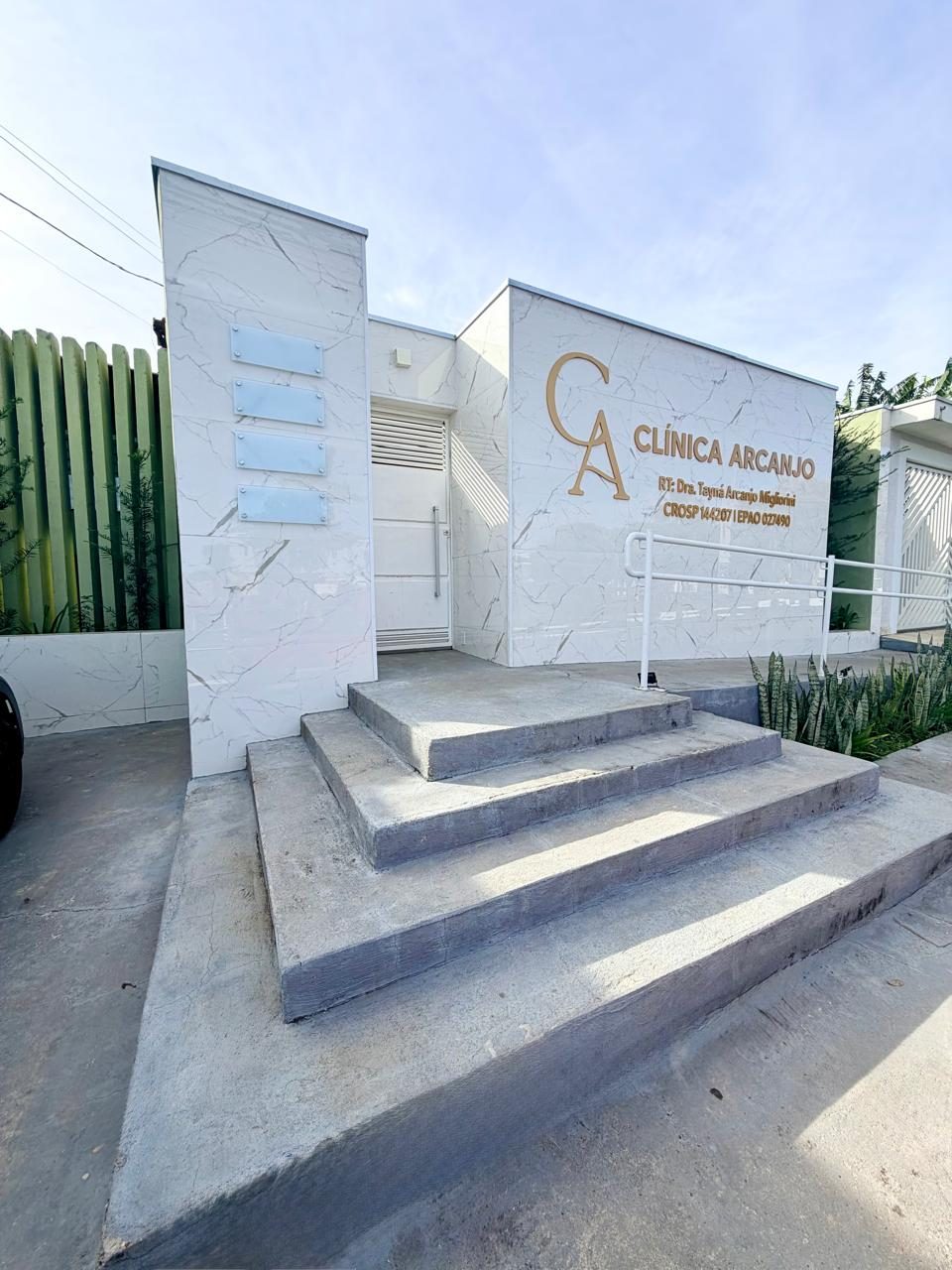 Fachada da Clínica Arcanjo, em mármore branco com a logo dourada e escada de acesso